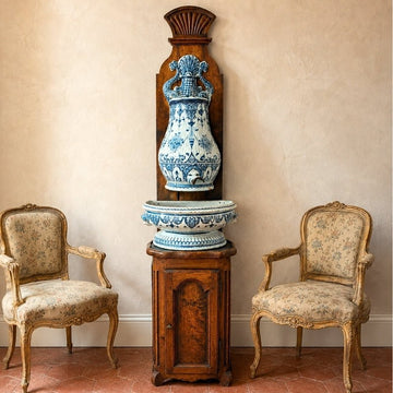 Antique French blue and white faïence wall fountain with basin displayed on carved wood between two Louis-style armchairs.