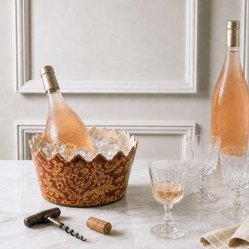 Ornate antique French ice bucket filled with ice and rosé, styled with crystal glasses and a corkscrew on a marble table.