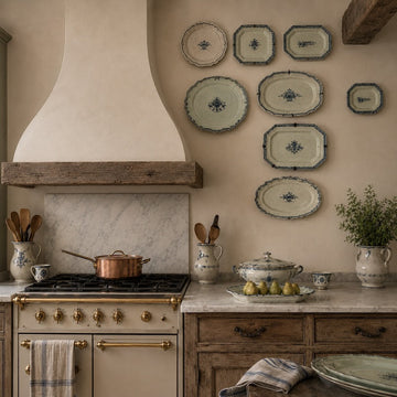 A rustic kitchen with wooden cabinets, a marble countertop, vintage stove, copper pot, and decorative plates on the wall. Fresh pears and utensils are neatly arranged, creating a cozy atmosphere.