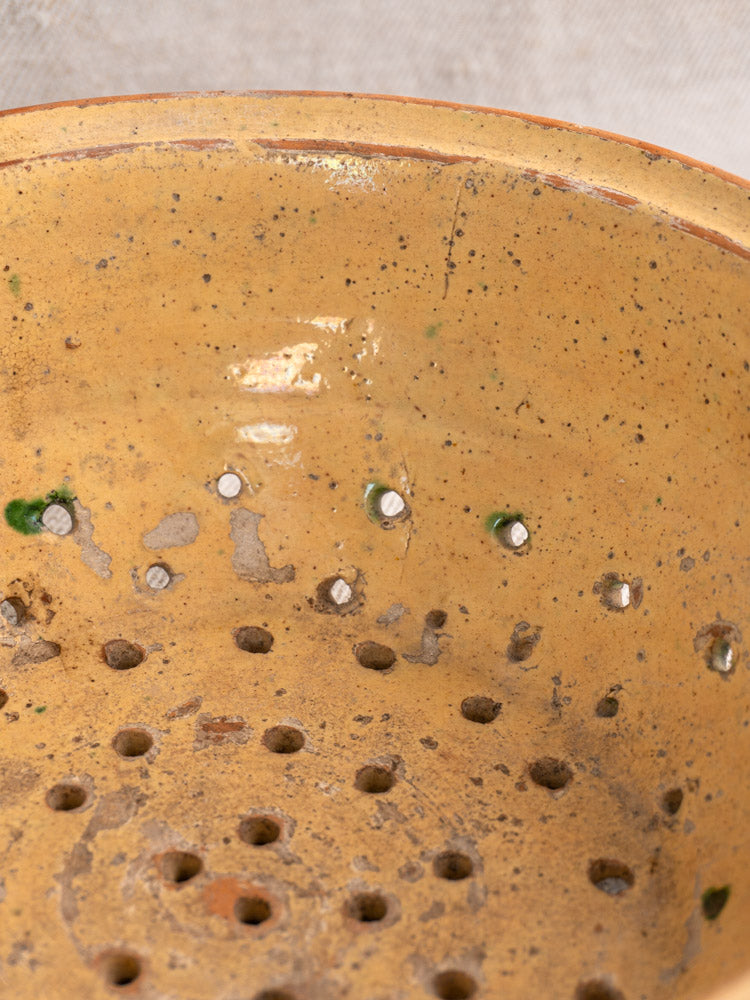 Antique French earthenware colander with jaspe glaze, yellow ceramic, green-brown spots, drainage holes, and aged patina.