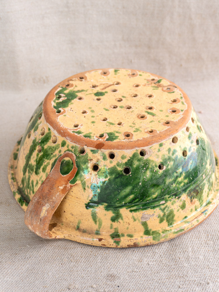 Antique French earthenware colander with jaspe glaze, yellow and green tones, aged chipped handle, late 19th century.