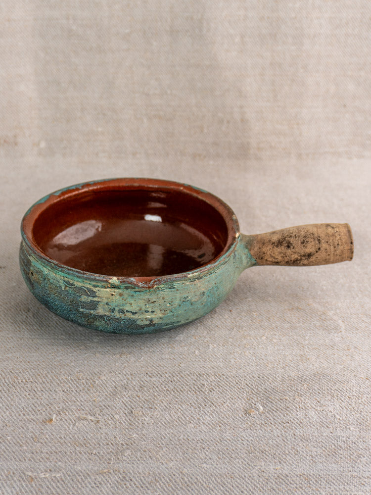 Antique French poêlon glazed earthenware pot with rounded shape, turquoise verdigris finish, on beige textured fabric.