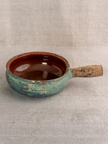 Antique French poêlon glazed earthenware pot with rounded shape, turquoise verdigris finish, on beige textured fabric.