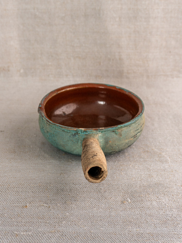 Antique French poêlon, small round glazed earthenware pot with brown interior, turquoise verdigris exterior, on textured fabric.