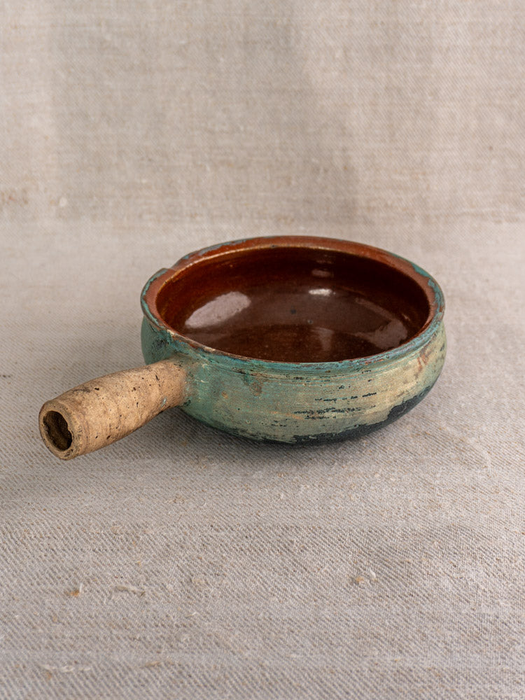 Antique French poêlon glazed earthenware pot, teal verdigris exterior, cork handle; displayed on neutral fabric.
