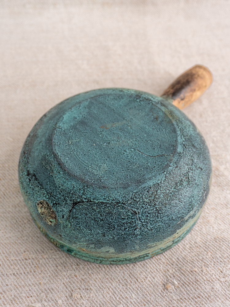 Antique French poêlon glazed earthenware cooking pot with verdigris patina, wooden handle, on textured fabric.