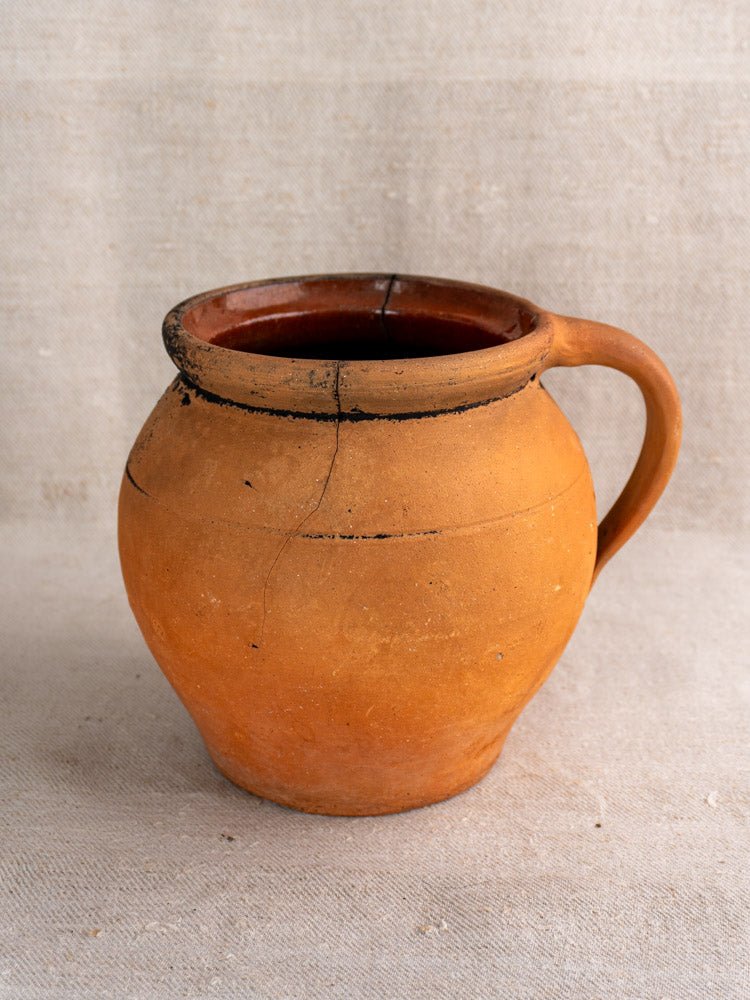 Antique French terracotta water jugs with fire-blackened patina and handles on beige fabric.