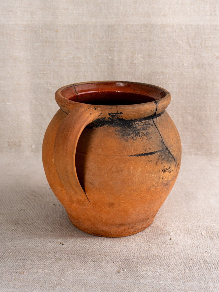 Pair of antique French terracotta cruches with fire-blackened patina on neutral fabric surface.