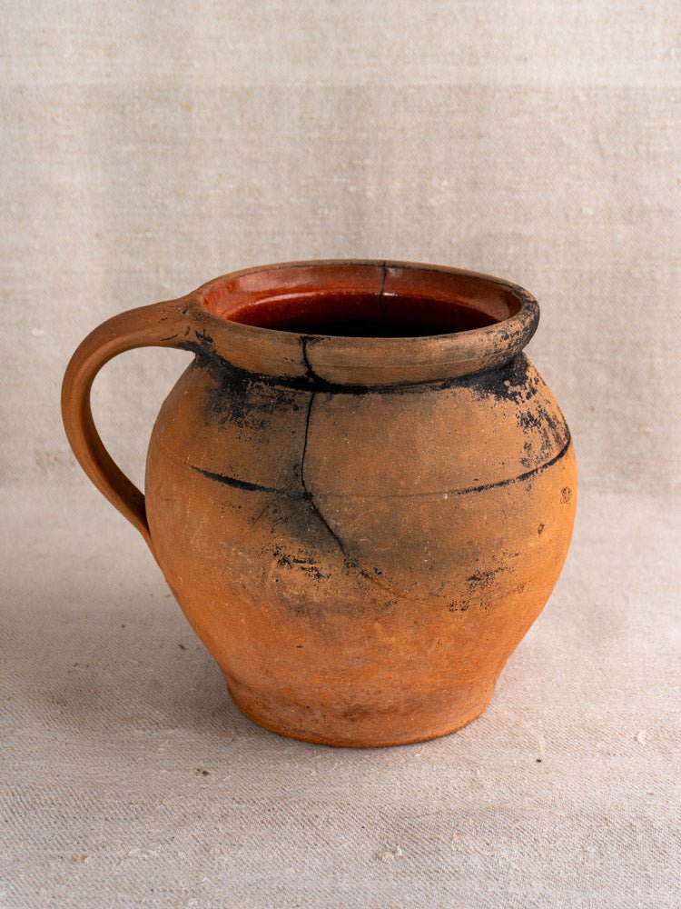 Pair of round, reddish-brown antique French cruche terracotta jugs with soot marks and cracks on fabric.