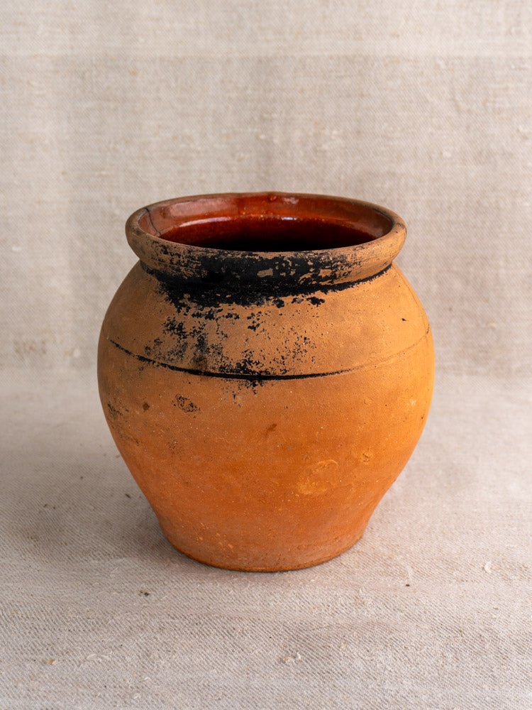 Pair of antique French terracotta cruches with fire-blackened patina on light fabric surface.