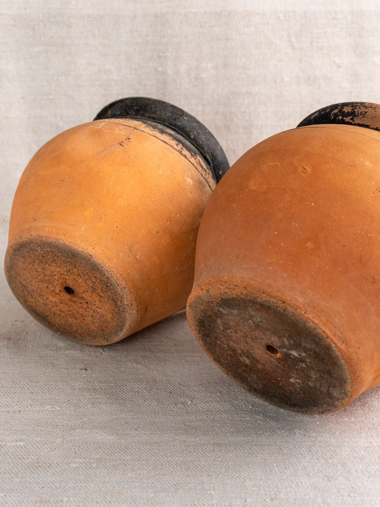 Pair of antique French terracotta cruche jugs with fire-blackened bases on neutral fabric.