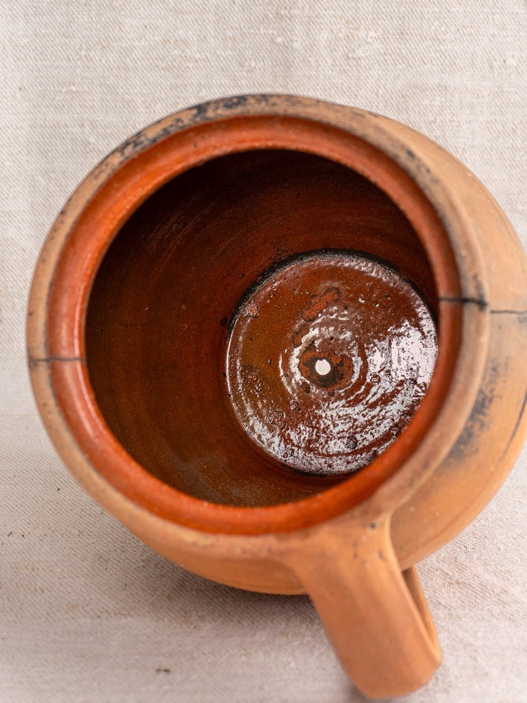Top view of antique French terracotta fire-blackened cruche with central base hole on textured fabric.