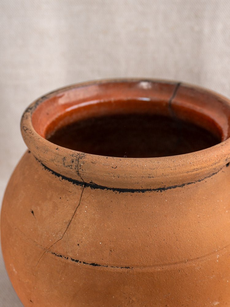 Antique French terracotta cruche with cracks, fire-blackened marks, and rich Provençal patina on light fabric.