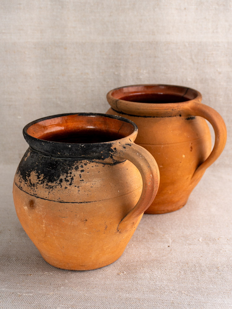 Pair of antique French fire-blackened terracotta cruches with handles on light textured fabric background.
