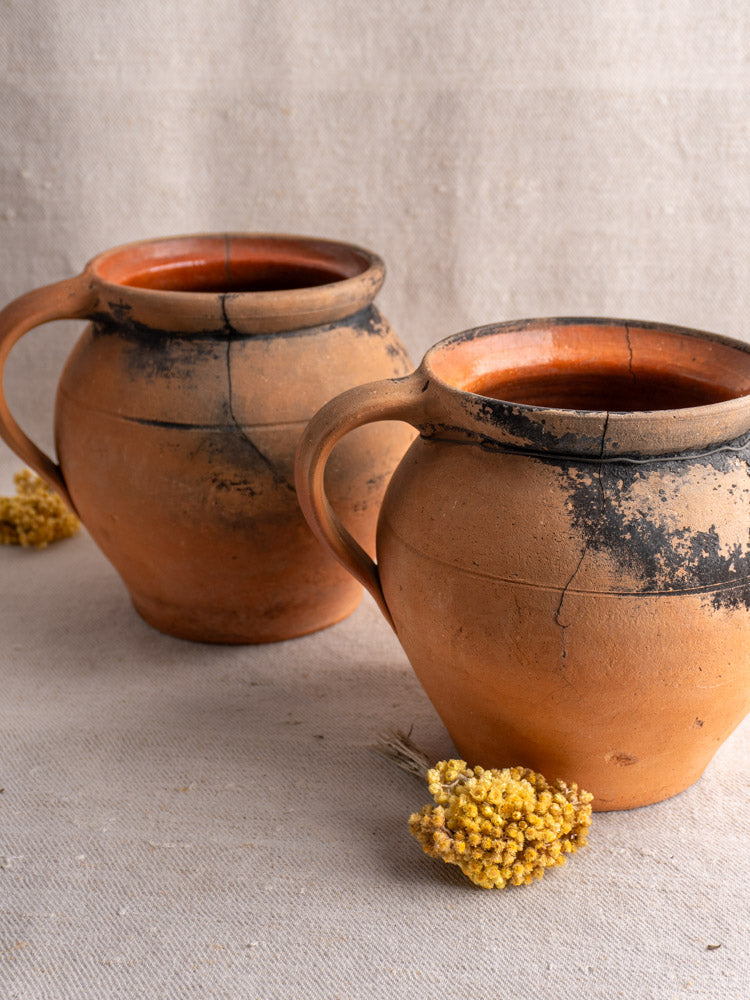 Pair of antique French fire-blackened terracotta cruches with handles on light textured fabric background.