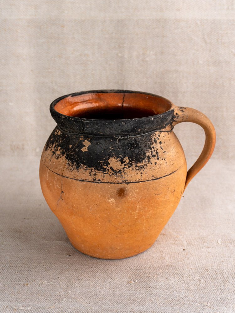 Pair of antique French terracotta cruche jugs with fire-blackened rims on textured fabric background.