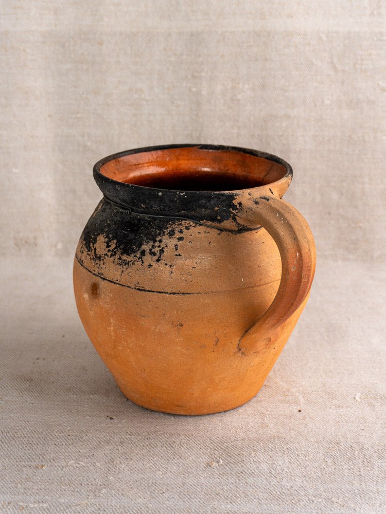 Pair of antique French terracotta cruches with blackened rims on beige textured fabric.