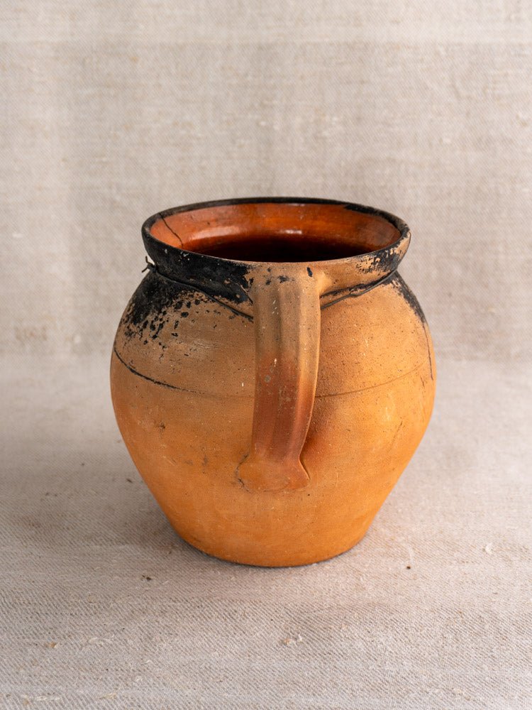 Pair of antique French terracotta cruches with fire-blackened rims on textured fabric background.