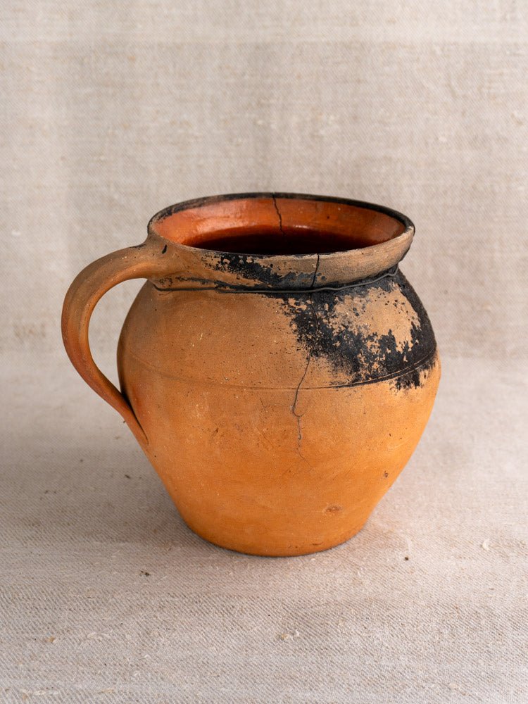 Pair of antique French terracotta water jugs with fire-darkened rims and warm orange clay on beige fabric.