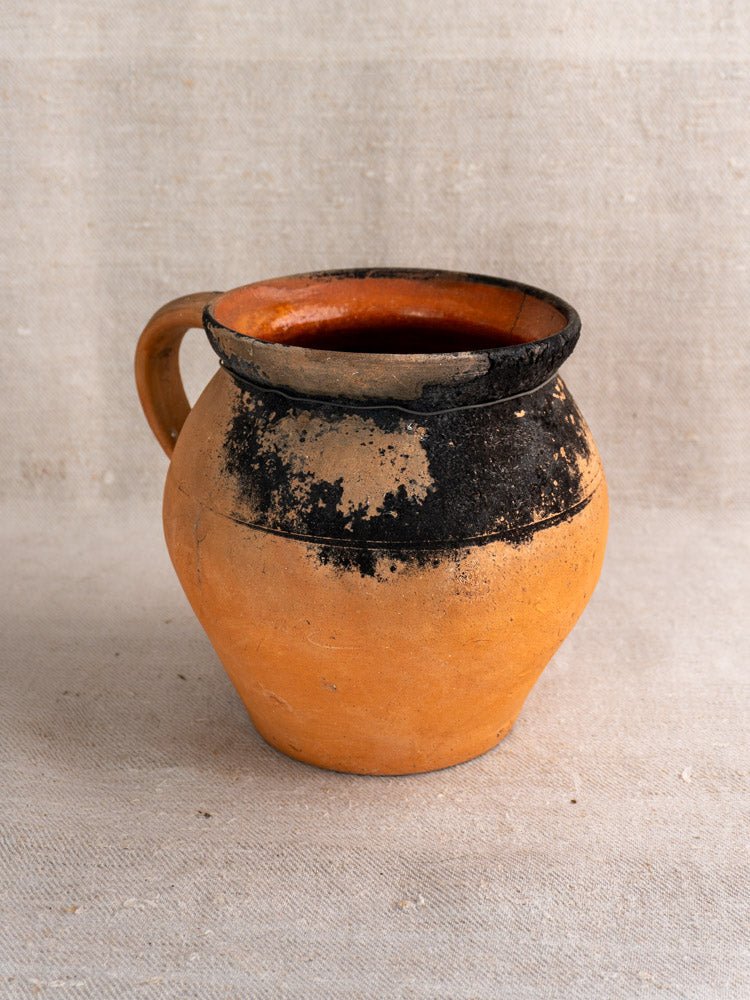 Pair of antique French terracotta cruches with fire-blackened rims on neutral fabric background.