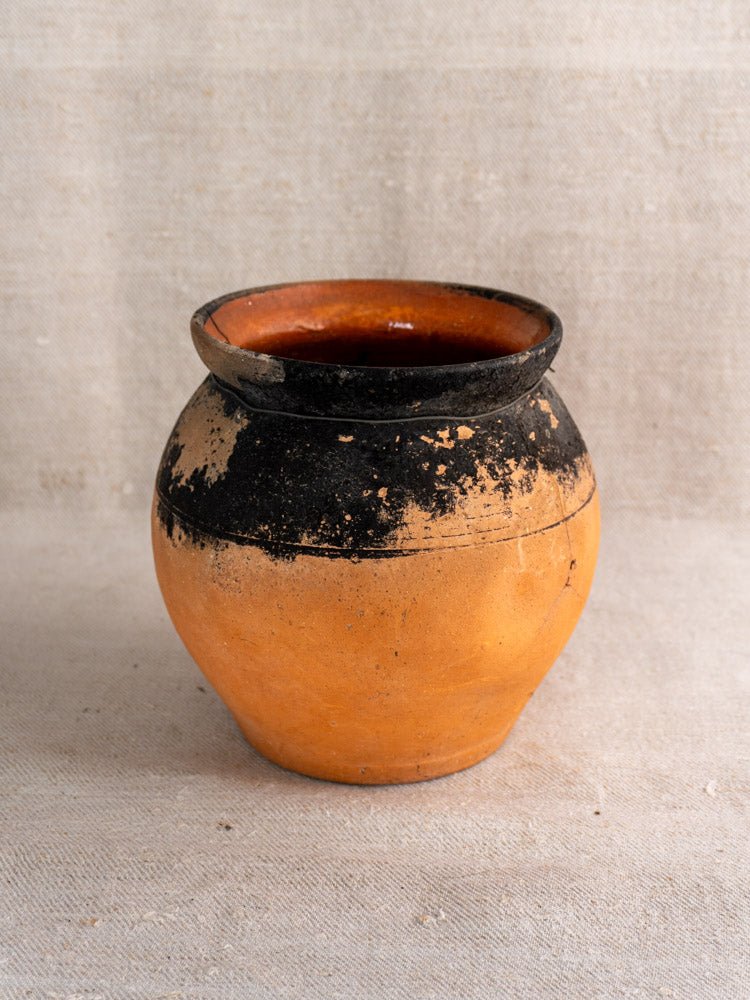 Pair of antique French terracotta cruches with fire-blackened tops on light textured fabric.