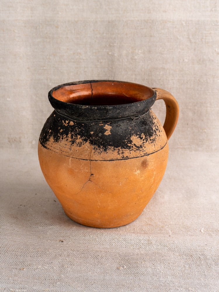 Pair of antique French terracotta cruches with fire-blackened tops on textured beige fabric.