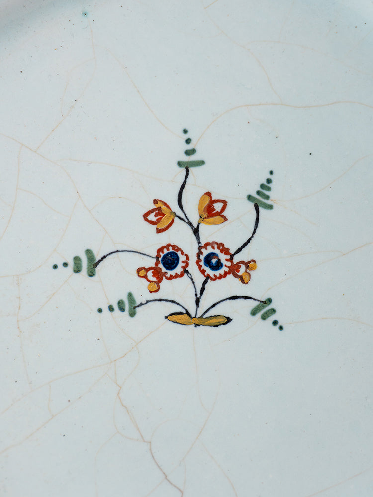 18th-century Moustiers French faience plate featuring polychrome orange and blue floral motif on a white, crackled ceramic surface.