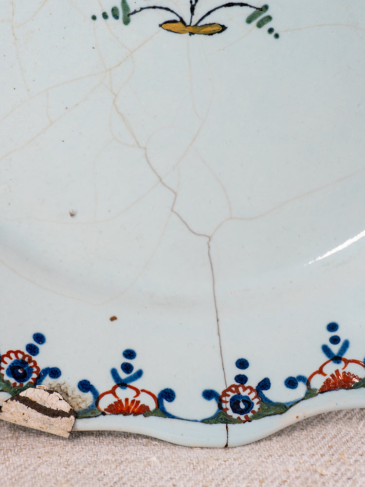 Antique 18th-century French faience plate with polychrome floral rim, cracked edge, and chipped tin-glazed enamel.
