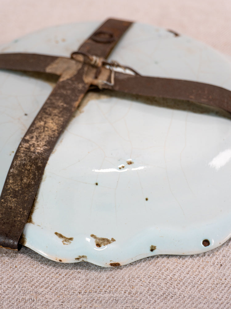 Antique French faience plate with polychrome floral design, cracked glaze, chips, and rustic metal repairs on beige fabric.