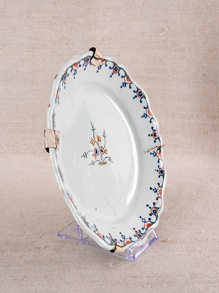 Antique French faience plate with scalloped rim and central polychrome floral bouquet on neutral fabric background.