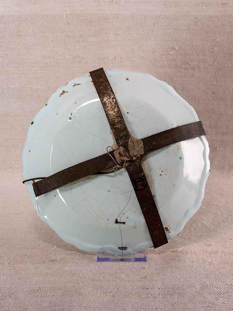 18th century French faience plate, Moustiers, polychrome floral, cracked with rusty cross brace, on beige textured background.