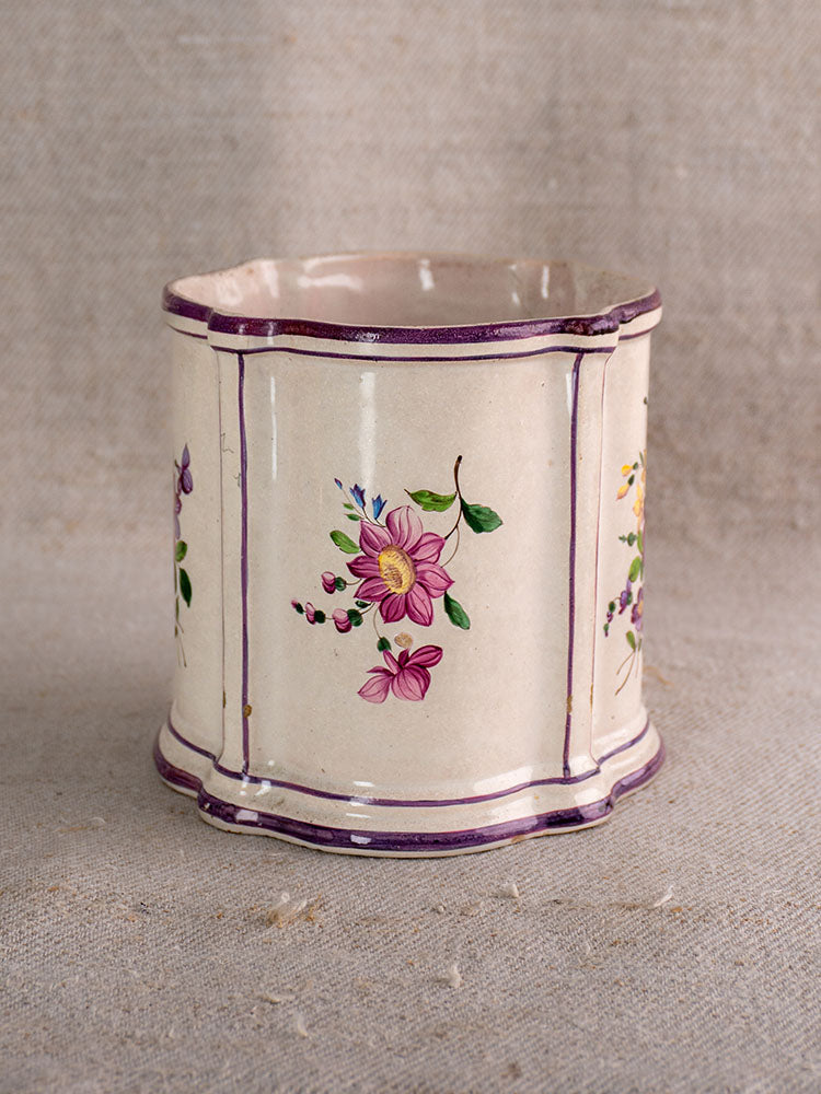 18th-century French faience cache pot with purple trim and chinoiserie flowers on beige textured fabric background.