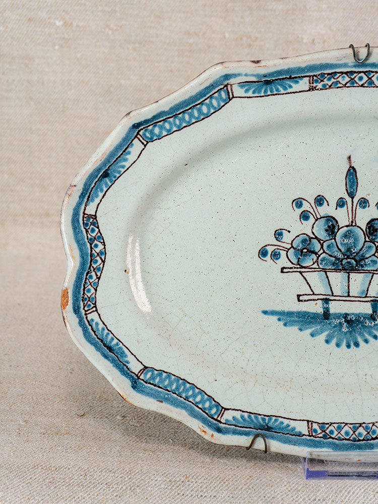 Antique French faience platter in Rouen Cul Noir style with scalloped edge, blue floral motif, border pattern, and visible wear.