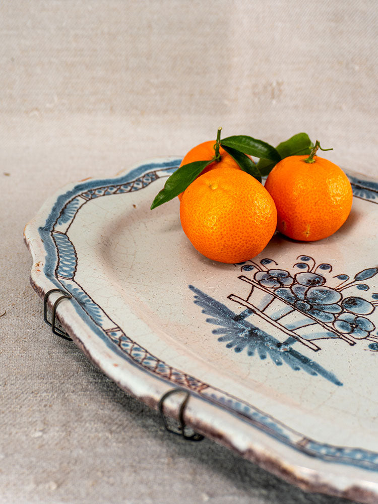 Antique French faience platter, Rouen Cul Noir style, with blue patterns and fruit motif, holding three oranges.