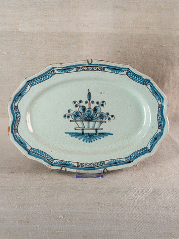 Antique French faience platter with scalloped edges, blue floral basket motif, on a neutral textured fabric background.
