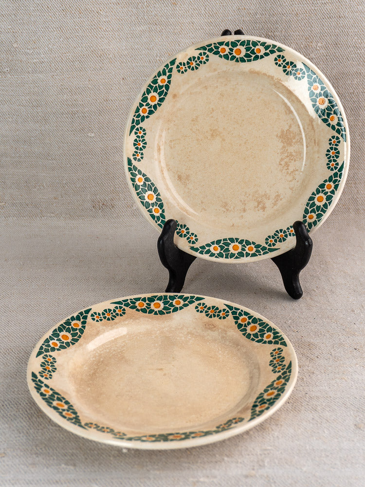 Antique French faience plate set, Trebeurden pattern, cream with green floral borders and orange accents, displayed on fabric.