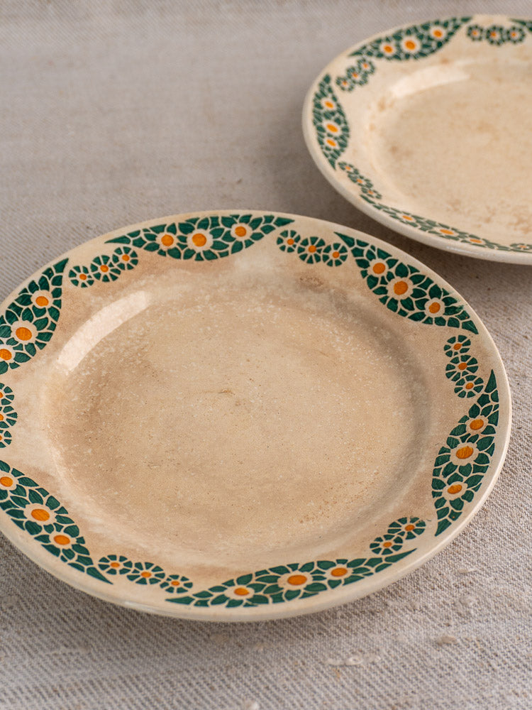 Pair of beige French faience plates with green and yellow floral rims on textured light grey fabric.