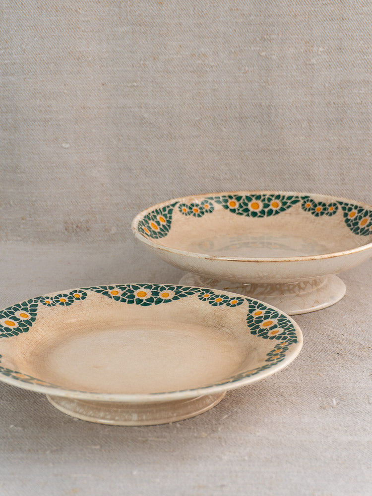 Antique French faience pedestal plate set with green and yellow geometric floral rims on neutral surface.
