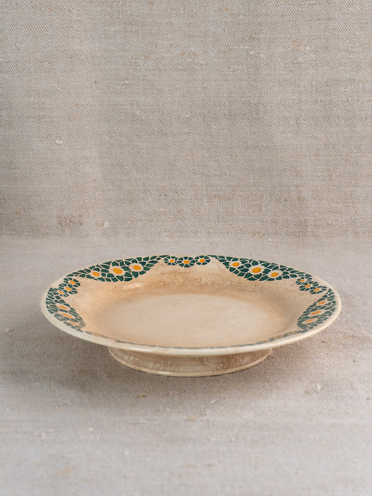 Antique French faience plate, HBCM Creil Montereau Trebeurden pattern, green-yellow floral rim, on beige textured fabric.