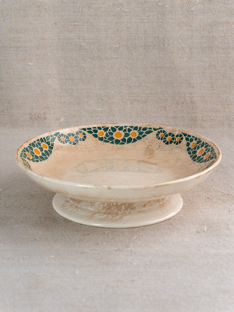 Antique French faience plate set by HBCM Creil Montereau, Trebeurden pattern, on textured beige fabric backdrop.