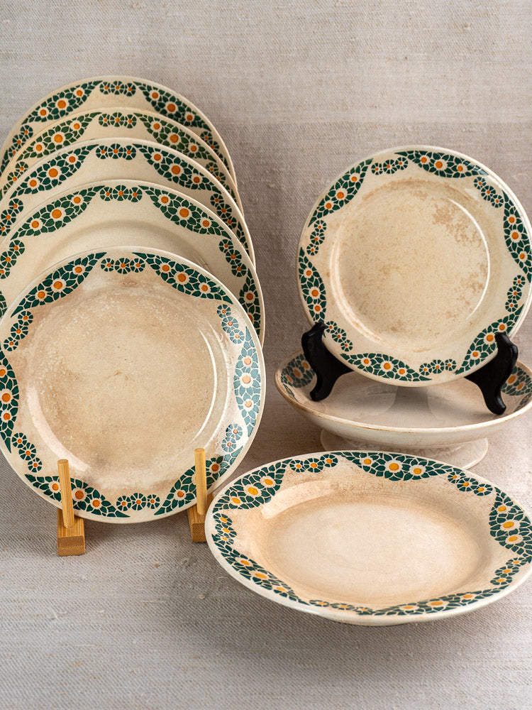 Antique French faience plate set by HBCM Creil Montereau, Trebeurden pattern, green-orange floral border, vintage wear, atop beige fabric.