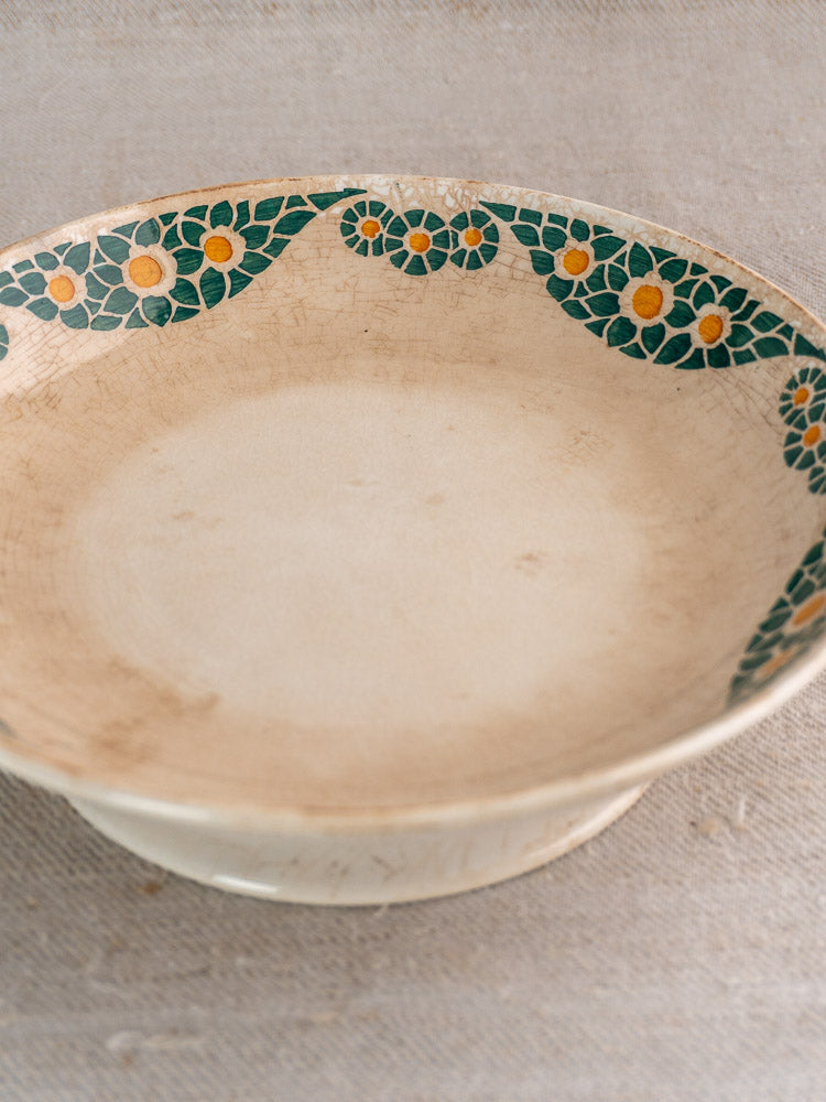 Antique French faience bowl, Trebeurden pattern with green leaves and yellow flowers, on textured beige surface.