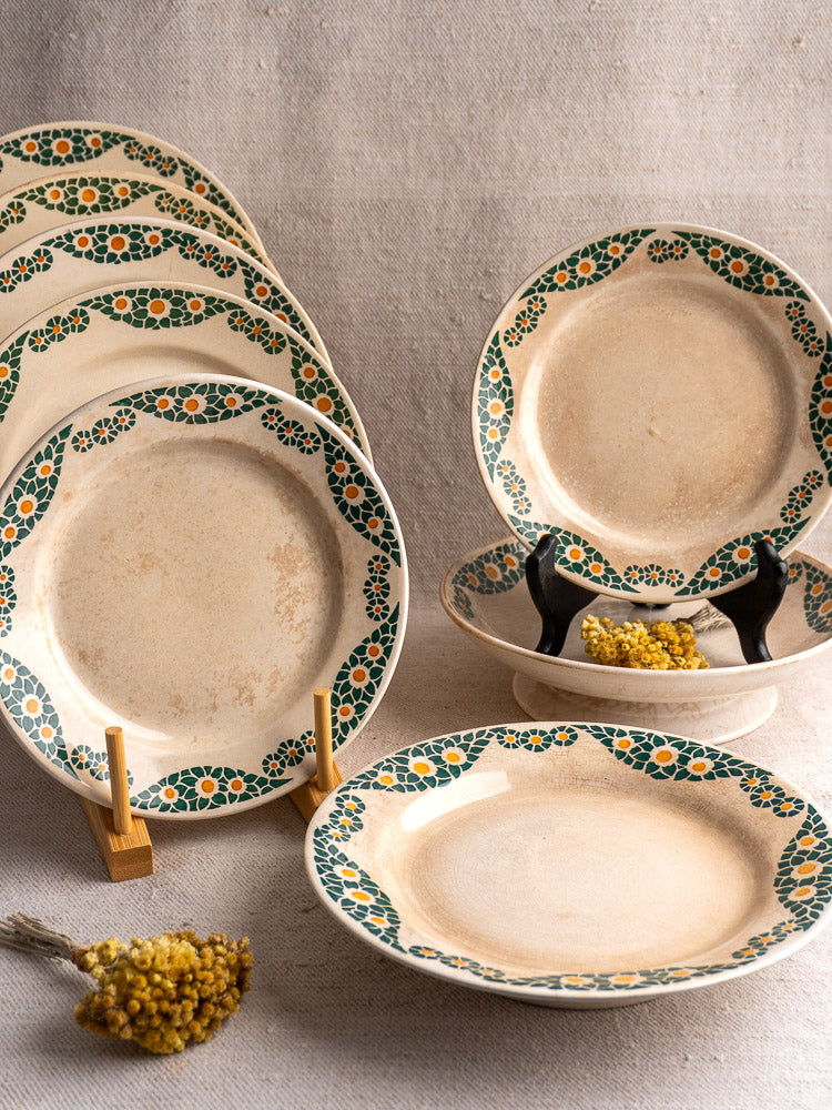 Antique French faience plate set, HBCM Creil Montereau Trebeurden, green and orange floral border, on neutral fabric with yellow flowers.