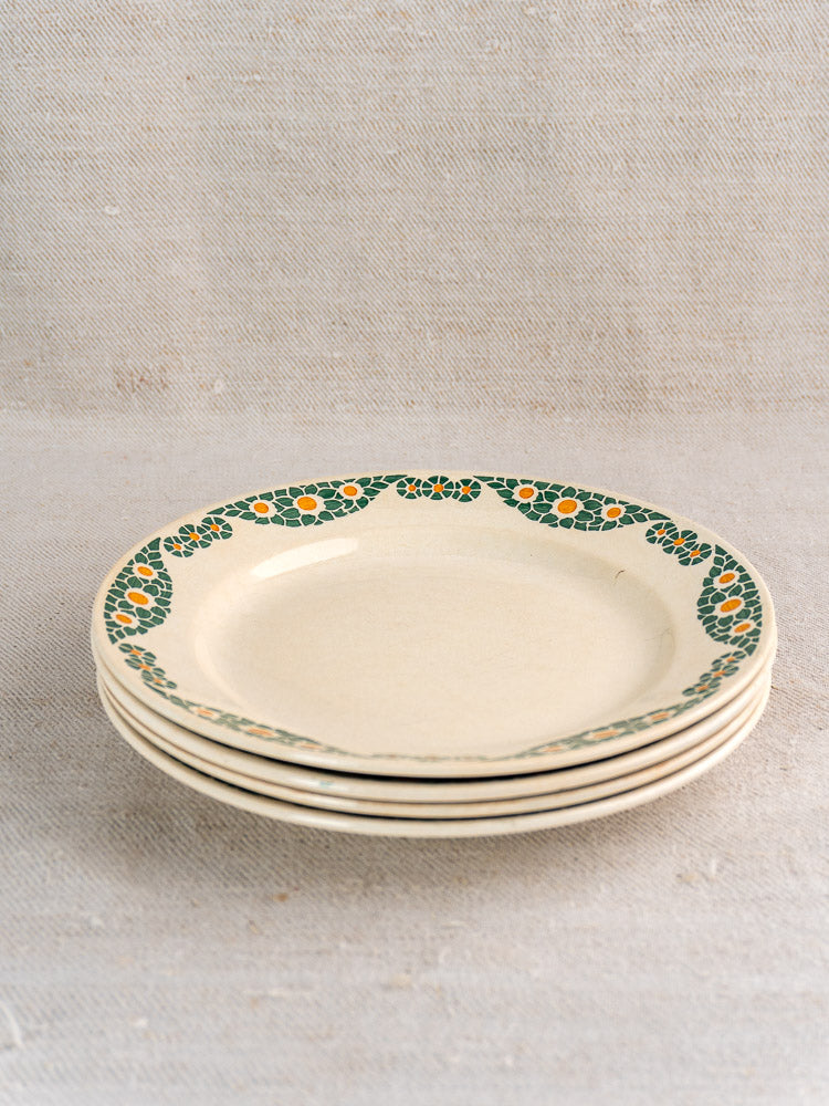Stack of three antique French faience plates, Trebeurden pattern, green and yellow floral rim, on neutral fabric surface.