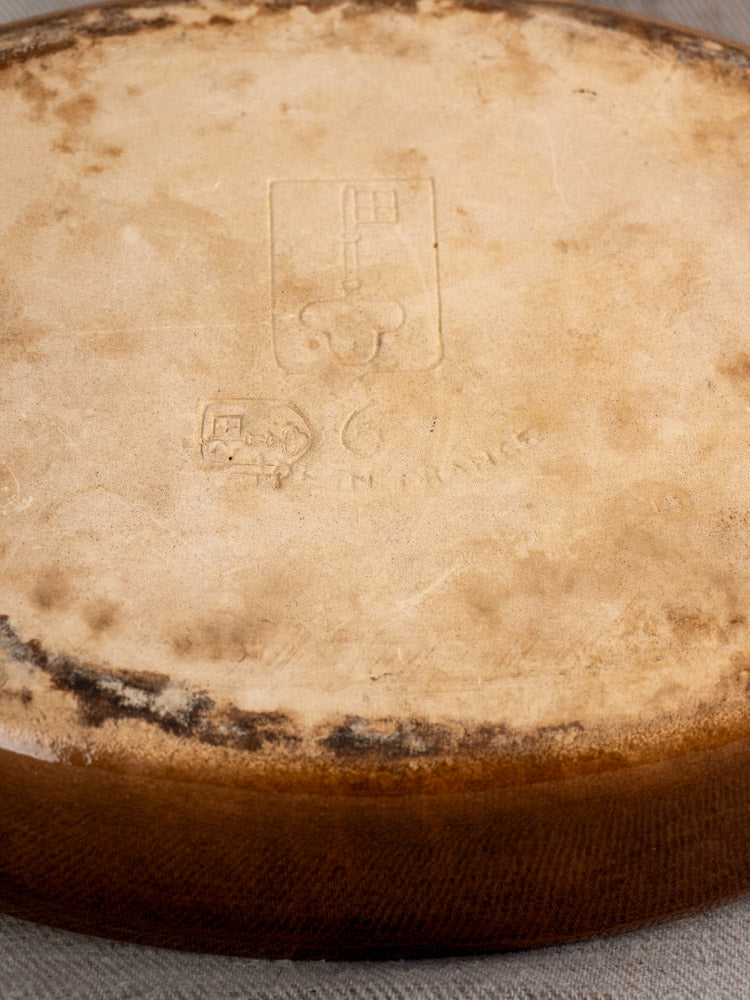 Browned, mottled rind of a round French cheese wheel with embossed key logo and faint text.