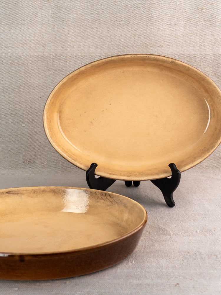 Pair of vintage French tan stoneware gratin dishes with glossy finish, one upright, one flat.