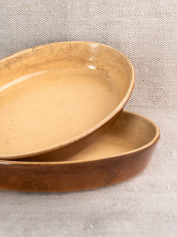 Matched pair of vintage French stoneware gratin dishes with brown glaze on light grey textured fabric.