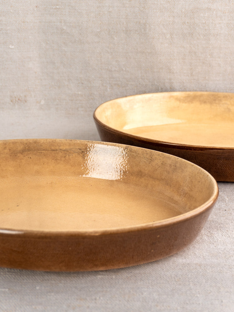 Pair of vintage French La Bourguignonne gratin dishes with brown stoneware exteriors and tan interiors on beige surface.