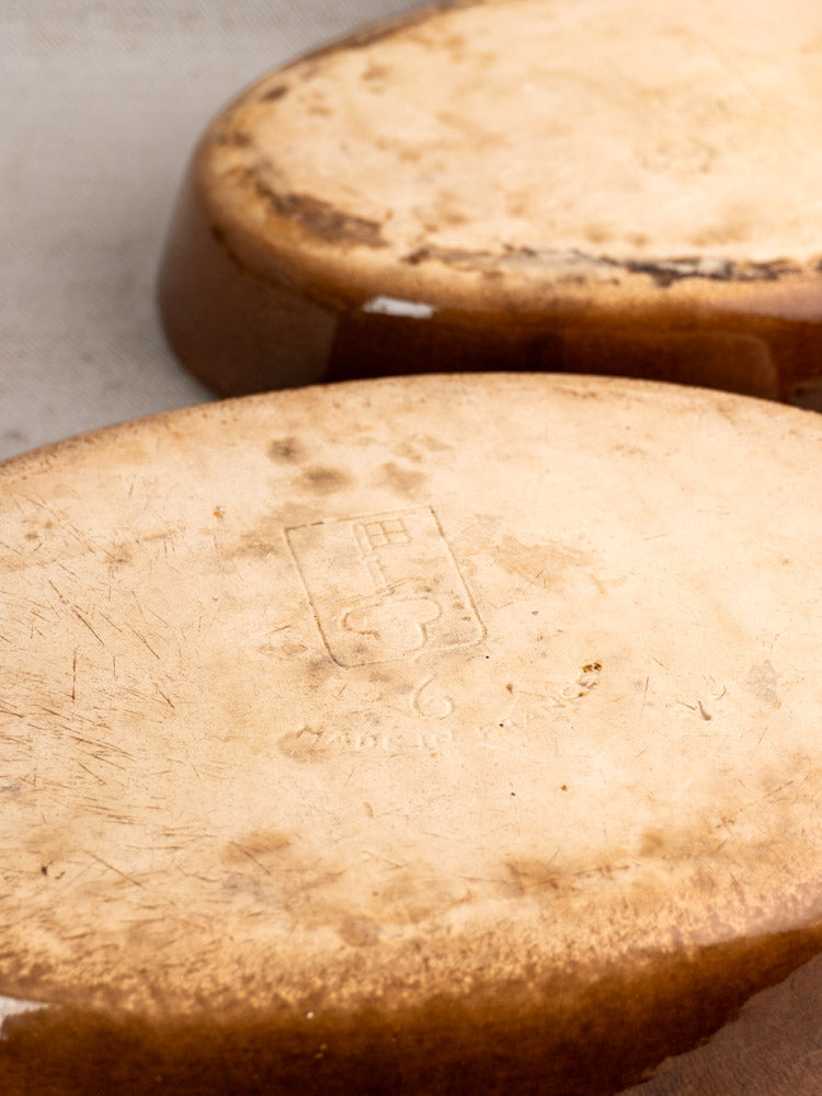 Pair of vintage French La Bourguignonne gratin dishes with tan stoneware bases, worn texture, and central stamped emblem.
