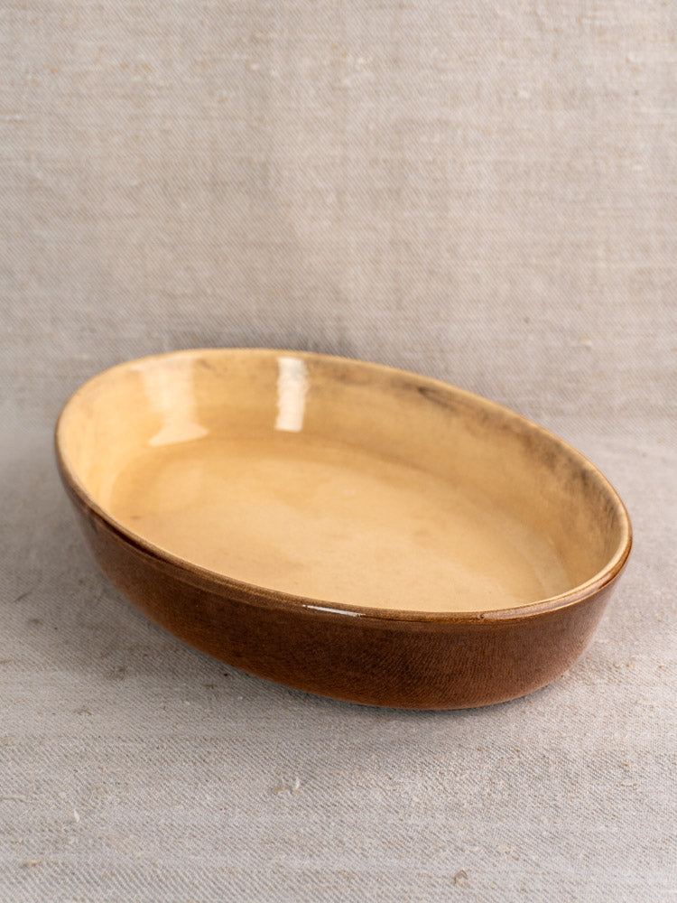 Pair of vintage French La Bourguignonne gratin dishes with beige interior on textured beige fabric.